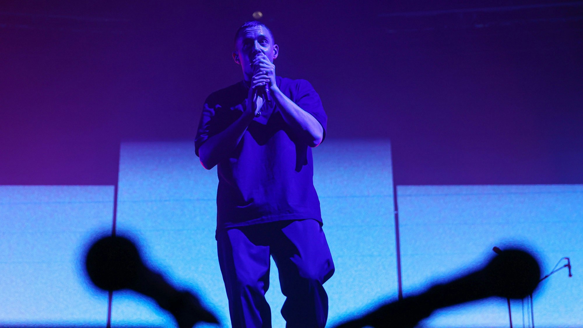 Sänger Dermot Kennedy steht auf der Bühne im Palladium. Er hält ein Mikrofon in der Hand. Zwei Mikrofone sind verschwommen im Vordergrund.