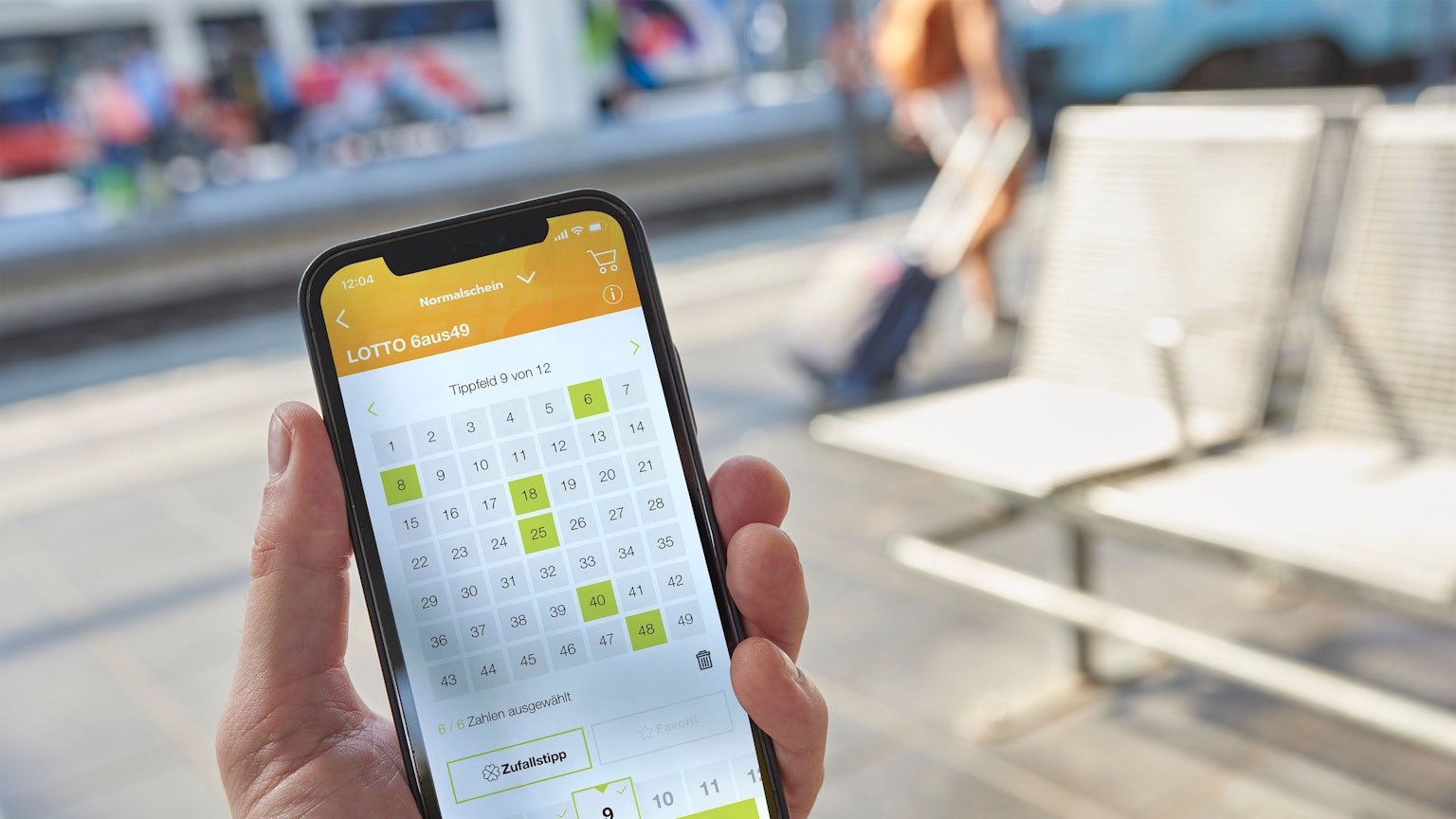 Mann hält Smartphone mit Lotto 6aus49 auf dem Display.