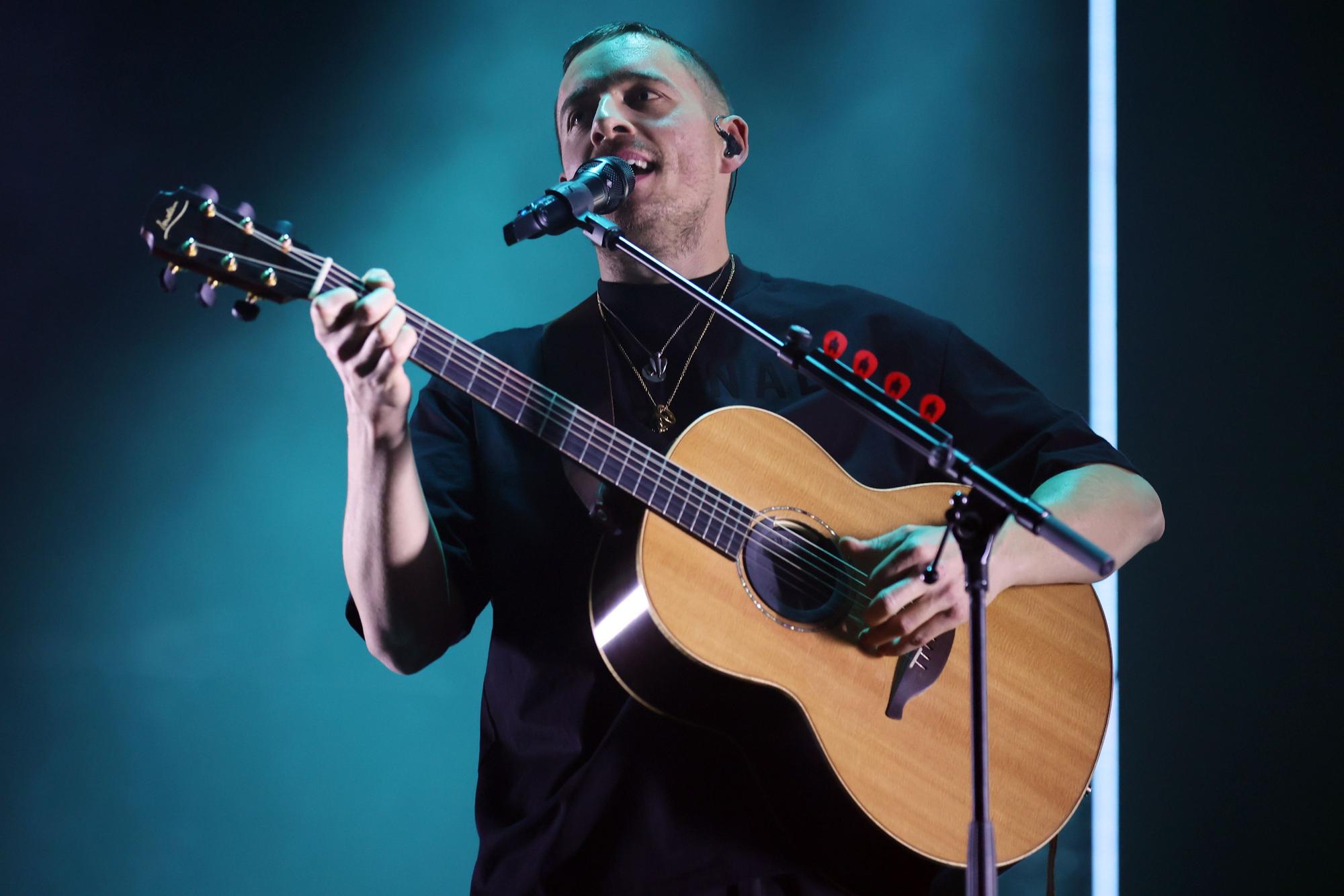 Dermot Kennedy steht mit Akustikgitarre auf der Bühne und singt in ein Standmikrofon.