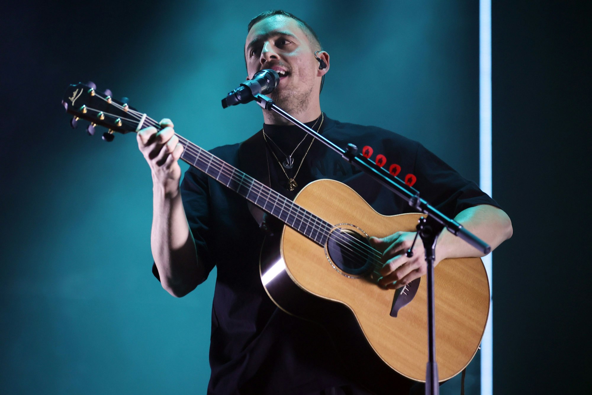 Dermot Kennedy steht mit Akustikgitarre auf der Bühne und singt in ein Standmikrofon.