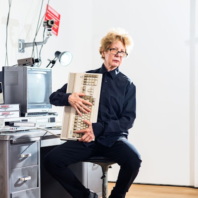 Julia Scher sitzt in ihrer Installation Information America und hält eine alte Computertastatur in den Händen.