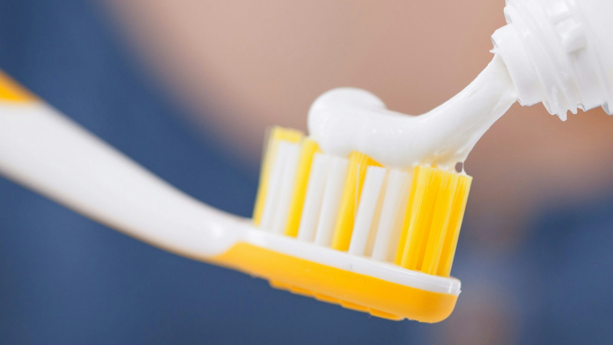 Eine Handzahnbürste in Nahaufnahme, gerade wird weiße Zahncreme auf sie gedrückt.
