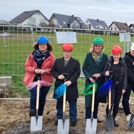 Mehrere Personen, darunter der Architekt Heinz Hennes und die Bürgermeisterin, stehen mit einem Spaten in der Hand auf dem Gelände der zukündtigen Kita.