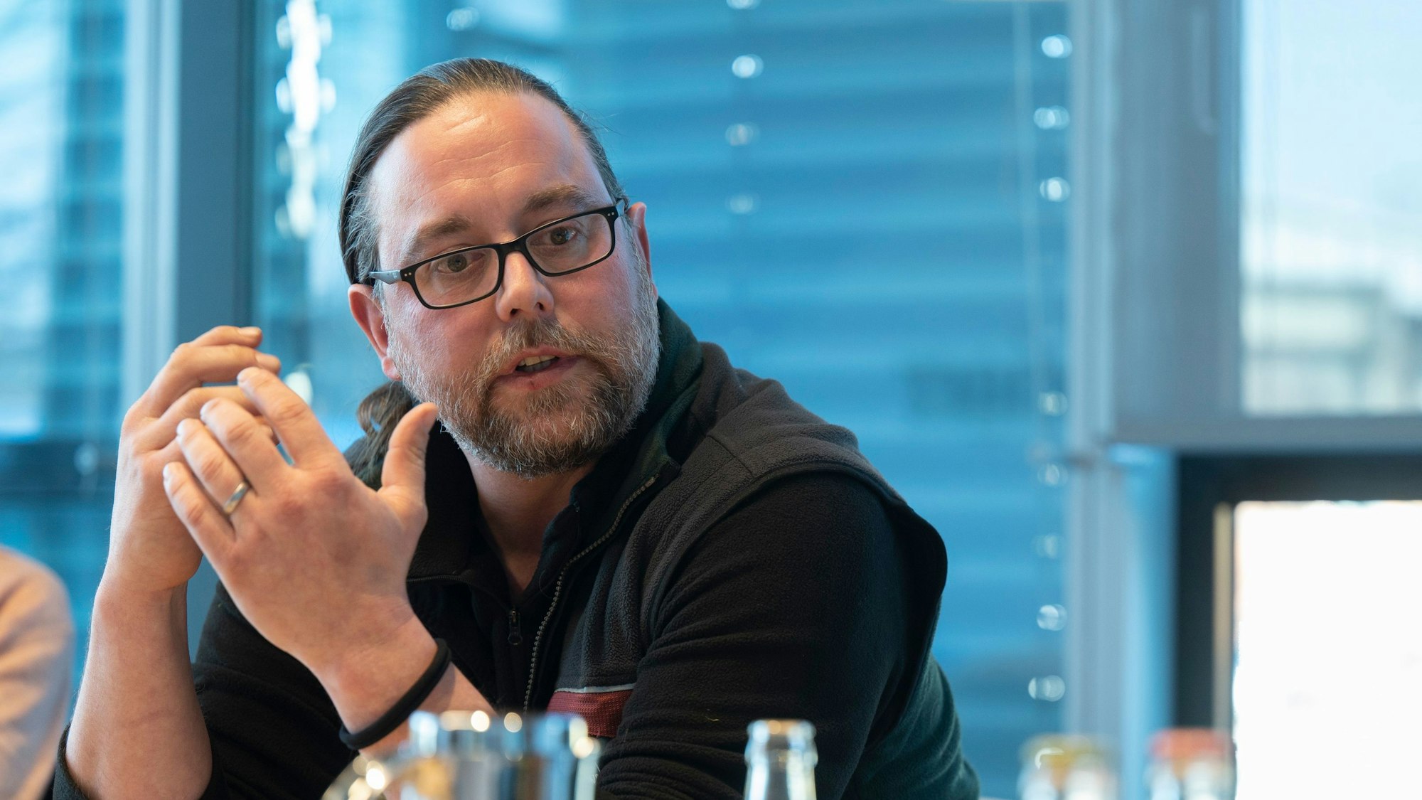 Wolfsberater Marc Redemann spricht während des Interviews beim Kölner Stadt-Anzeiger. Er sitzt an einem Tisch, trägt dunkle Kleidung, Bart und eine Brille. Seine Haare sind zu seinem Zopf zusammengebunden.