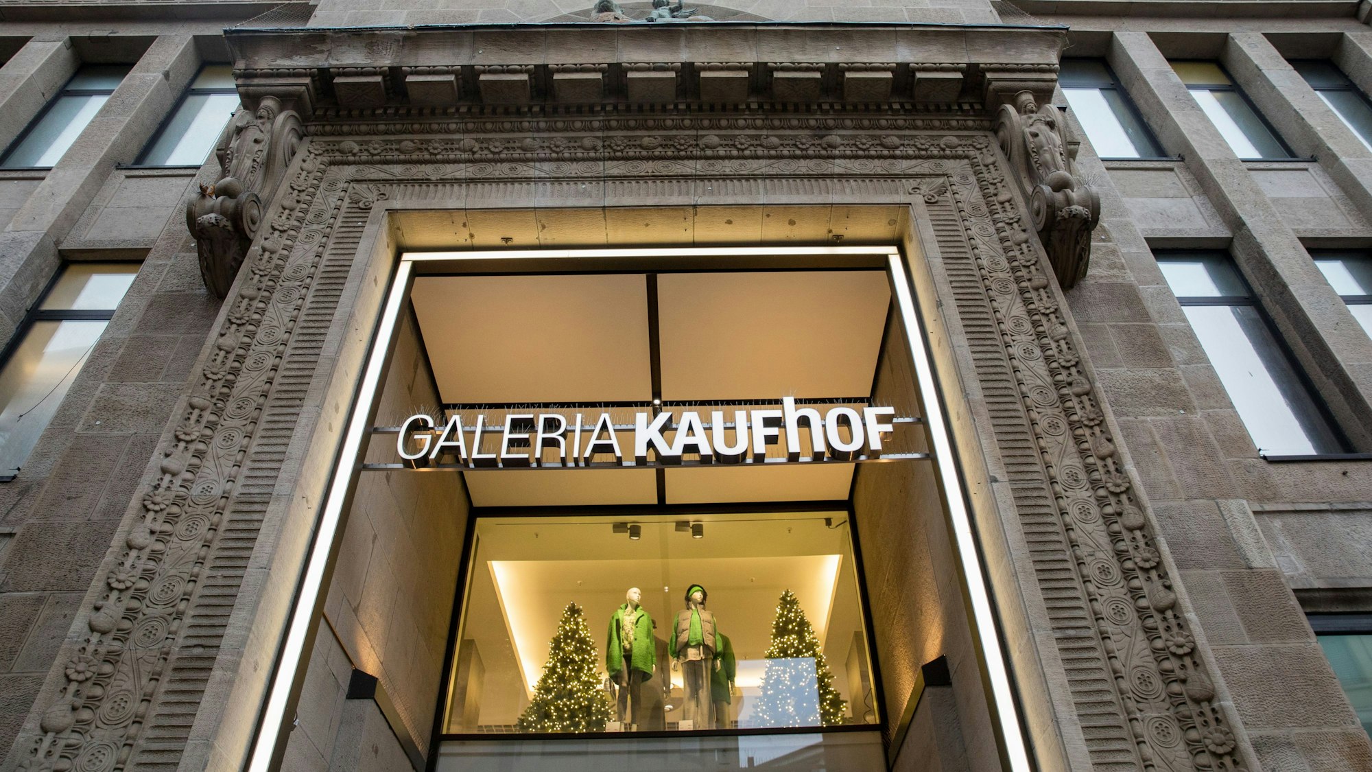 Außenansicht des Warenhauses Galeria Kaufhof in Köln. Über dem steinernen Eingangsportal ist der Schriftzug „Galeria Kaufhof“ zu sehen, darunter gibt das Portal einen Blick auf ein Schaufenster in der ersten Etage frei.