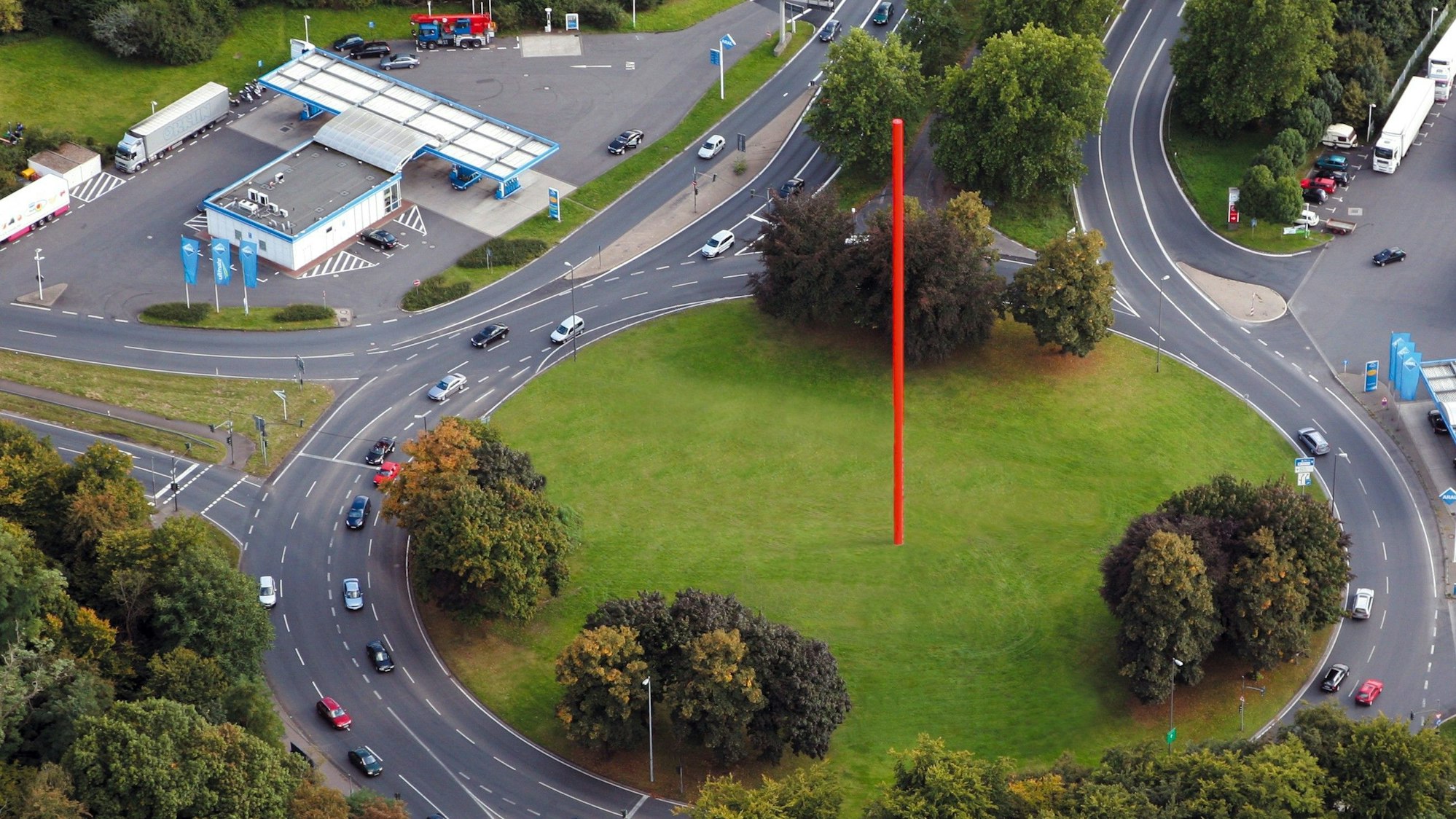 Eine riesige rote Stele steht in der Mitte eines begrünten Kreisverkehrs.