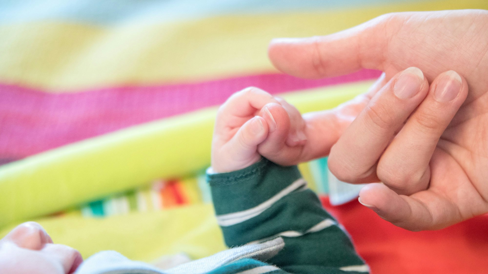 Eine Babyhand umklammert einen Zeigefinger.