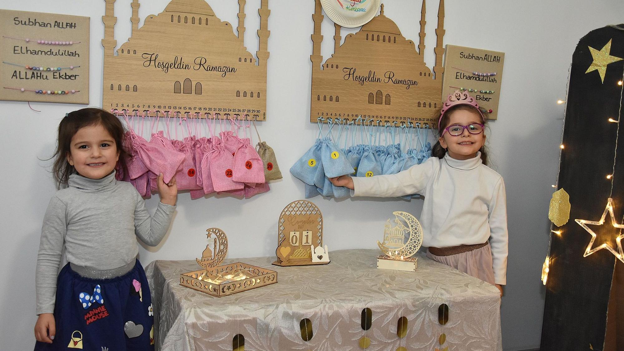 Zwei kleine Mädchen stehen vor Ramadan-Dekorationen. In dreißig Säckcken, die unter einem hölzernen Moschee-Schild aufgehangen sind, erwarten sie Geschenke.