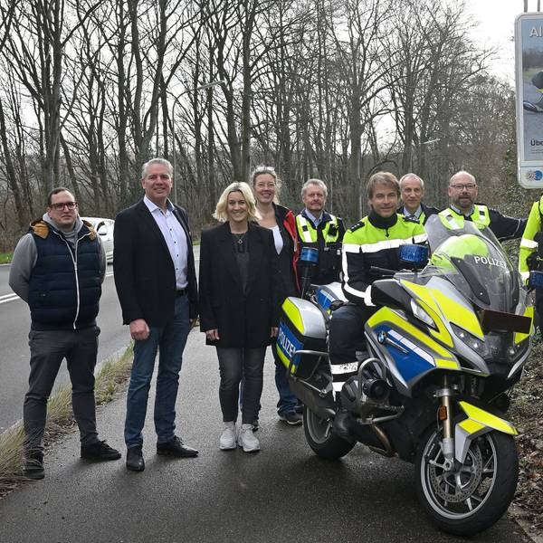 Polizeibeamtinnen und -beamte sowie Vertreter von Gemeinden, Städten und Kreis stehen vor einem neuen Schild, das Motorradfahrer zu Vorsicht anhalten soll. Über dem Bild eines verunglückten Motorrads ist der Schriftzug„ Alles im Griff?“ zu lesen.