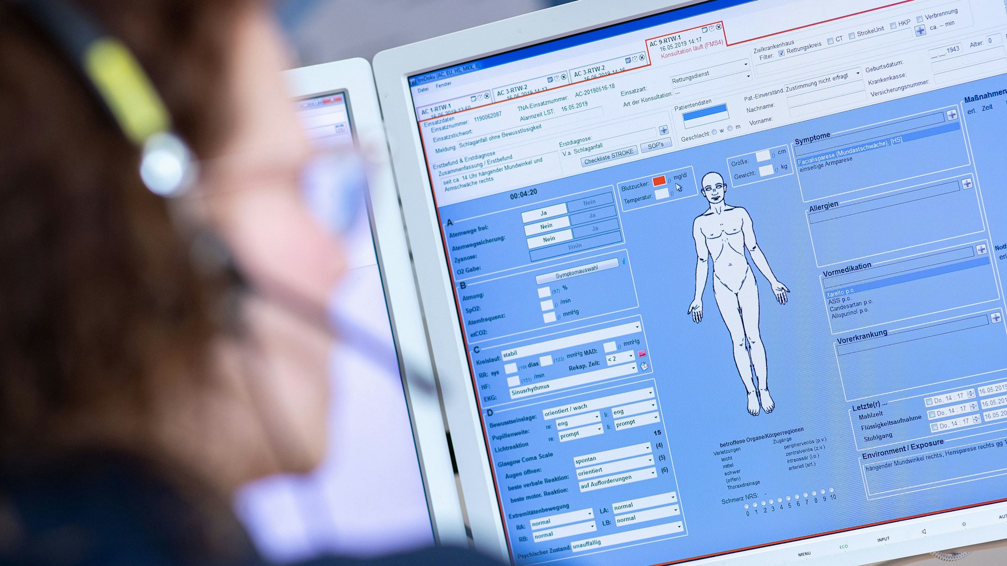 Eine Telenotärztin sitzt in der Rettungsleitstelle der Feuerwehr vor einem Bildschirm und ist mit Rettungssanitätern verbunden