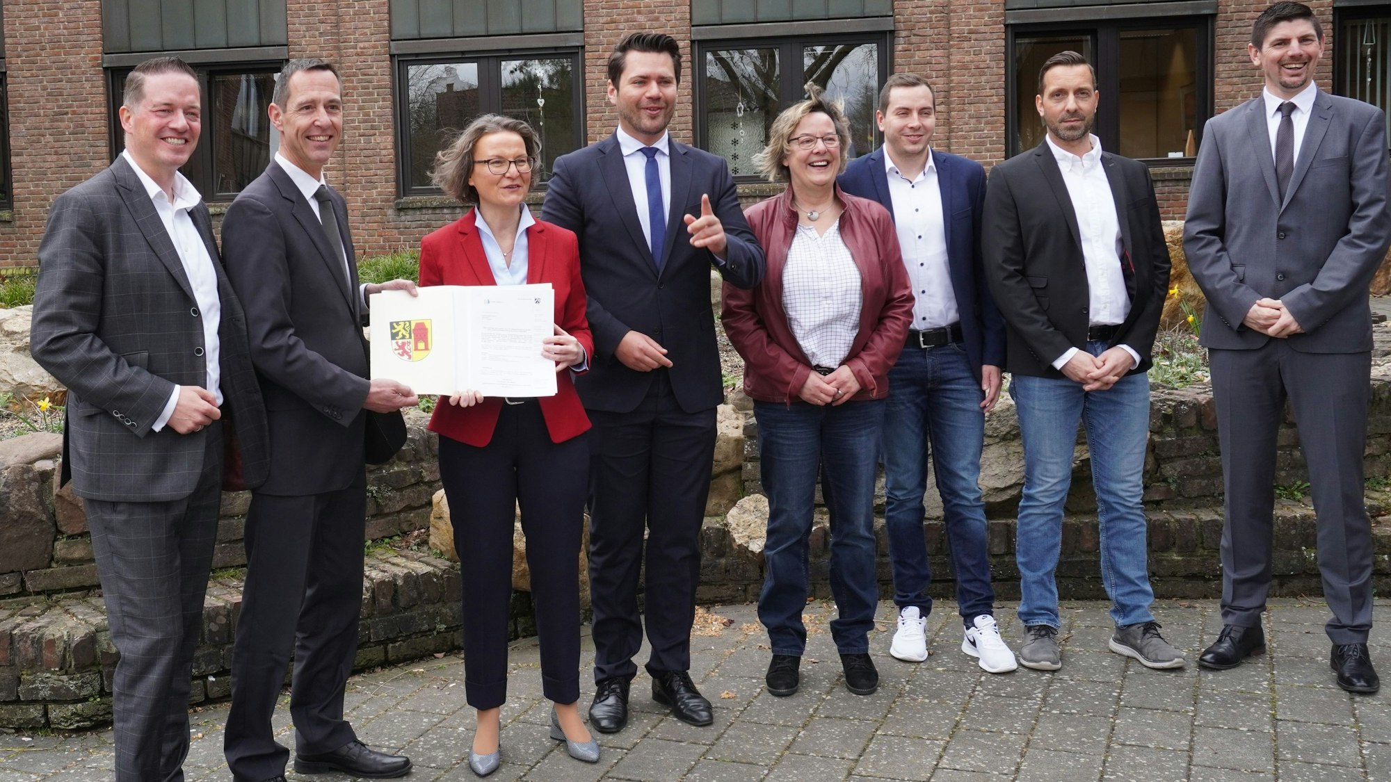 Eine Gruppe Männer und Frauen lächelt in die Kamera. Die NRW-Ministerin Ina Scharrenbach hält einen Förderbescheid.
