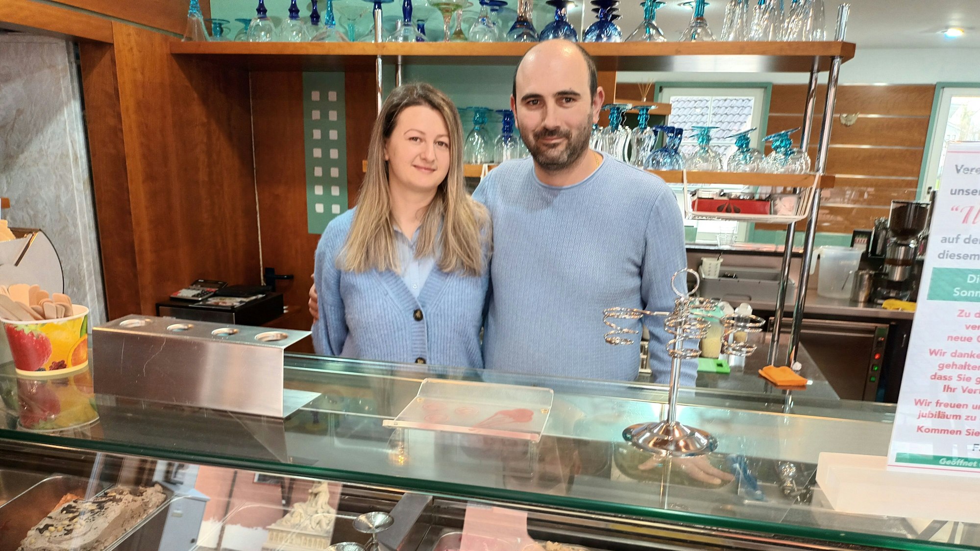 Zwei Personen stehen, sich in den Armen liegend, hinter einer Eistheke.