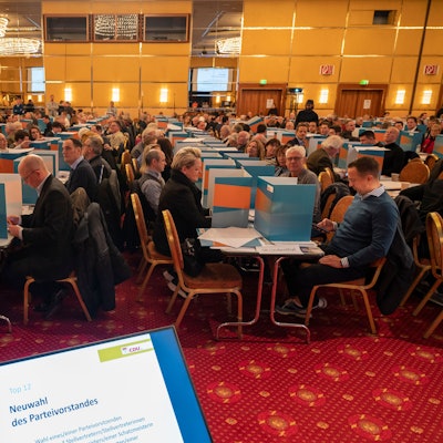 Das Bild zeigt hunderte Menschen, die in einem Saal an Tischen sitzen.