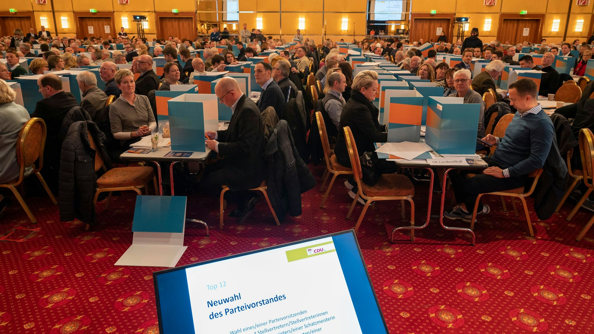 Das Bild zeigt hunderte Menschen, die in einem Saal an Tischen sitzen.