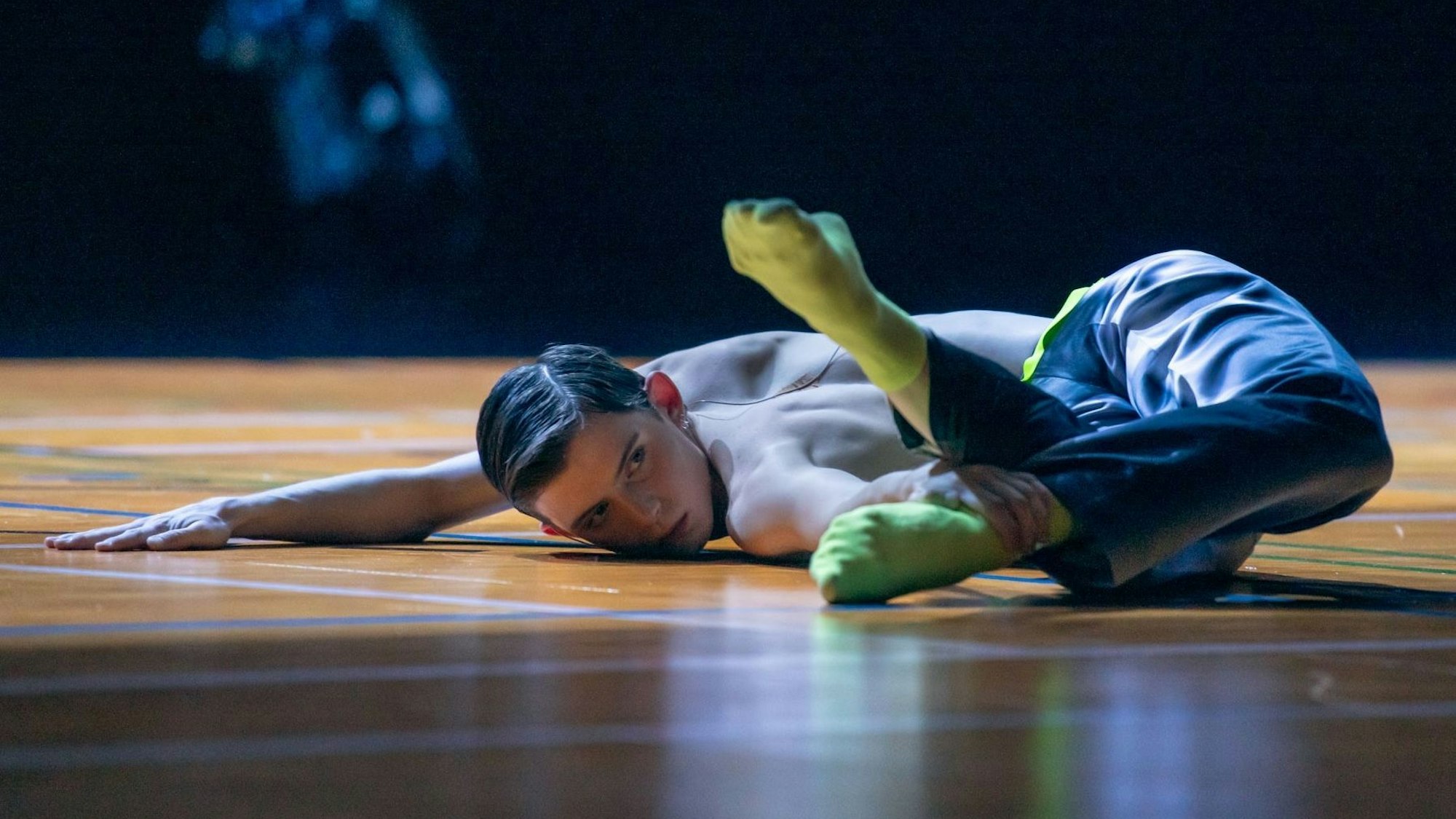 Szene aus „Ballet of (Dis)Obedience“ von Choreograf Richard Siegal. Ein Tänzer streckt sich am Boden. Einen Arm hat er ausgestreckt, den Unterkörper abgewinkelt. Mit der anderen Hand hält er einen Fußknöchel.