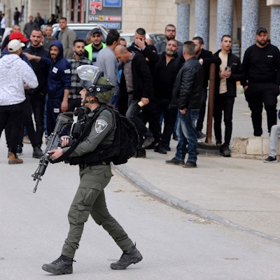 Ein Istraelischer Soldat läuft vor mehreren Demonstrierenden auf einer Straße.
