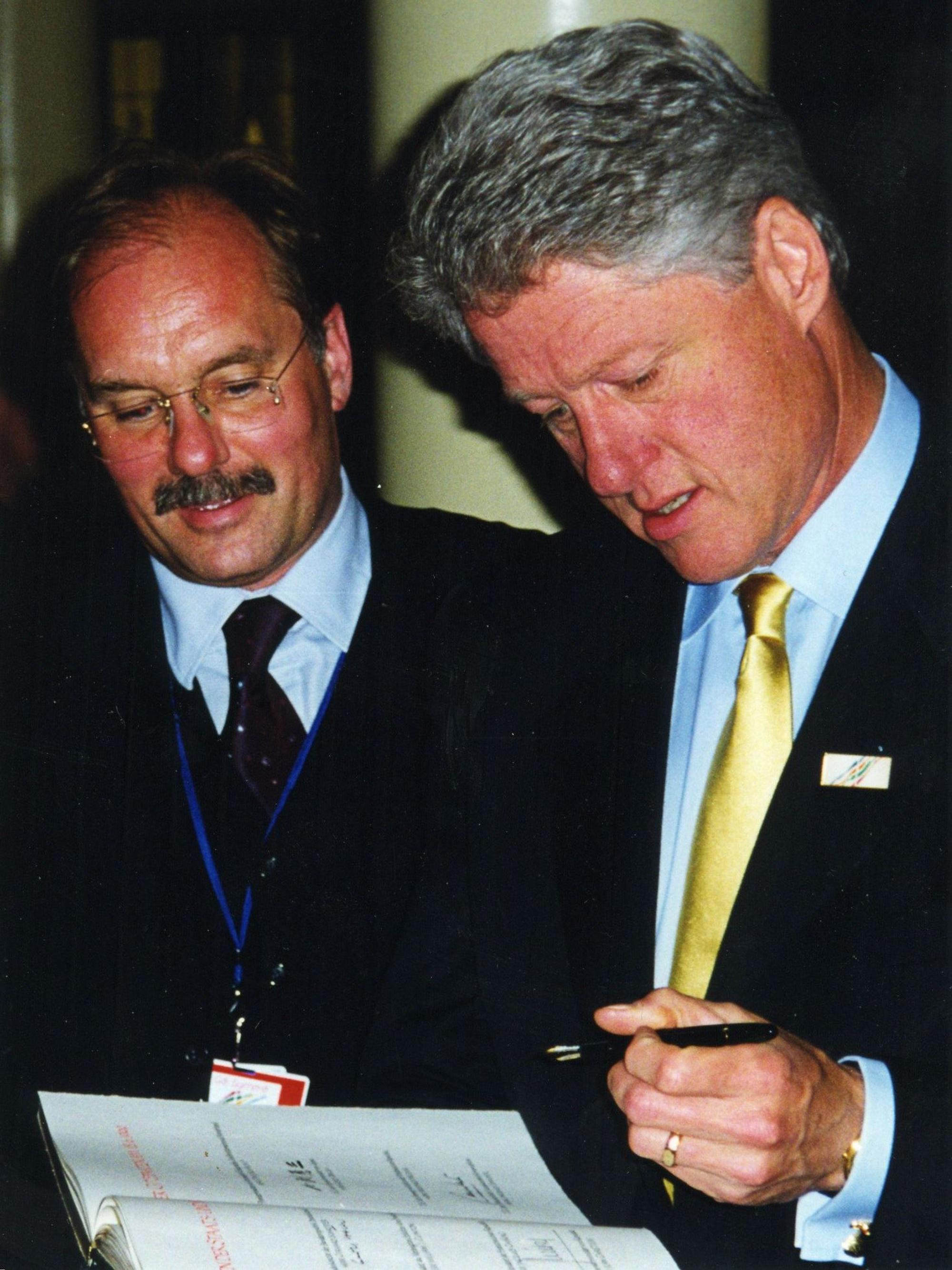 Bill Clinton hält ein Buch und einen Füller in den Händen, neben ihm steht Bernhard Conin.