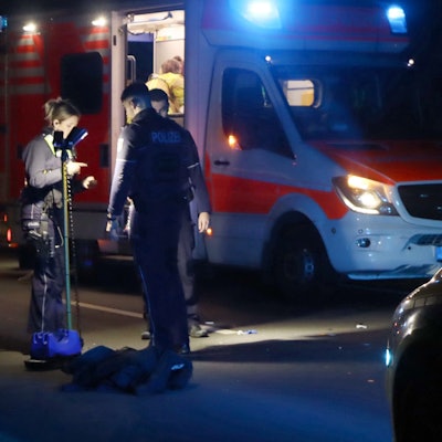 Es ist ein Rettungswagen zu sehen. Davor stehen mehrere Polizisten und Sanitäter an der Unfallstelle.