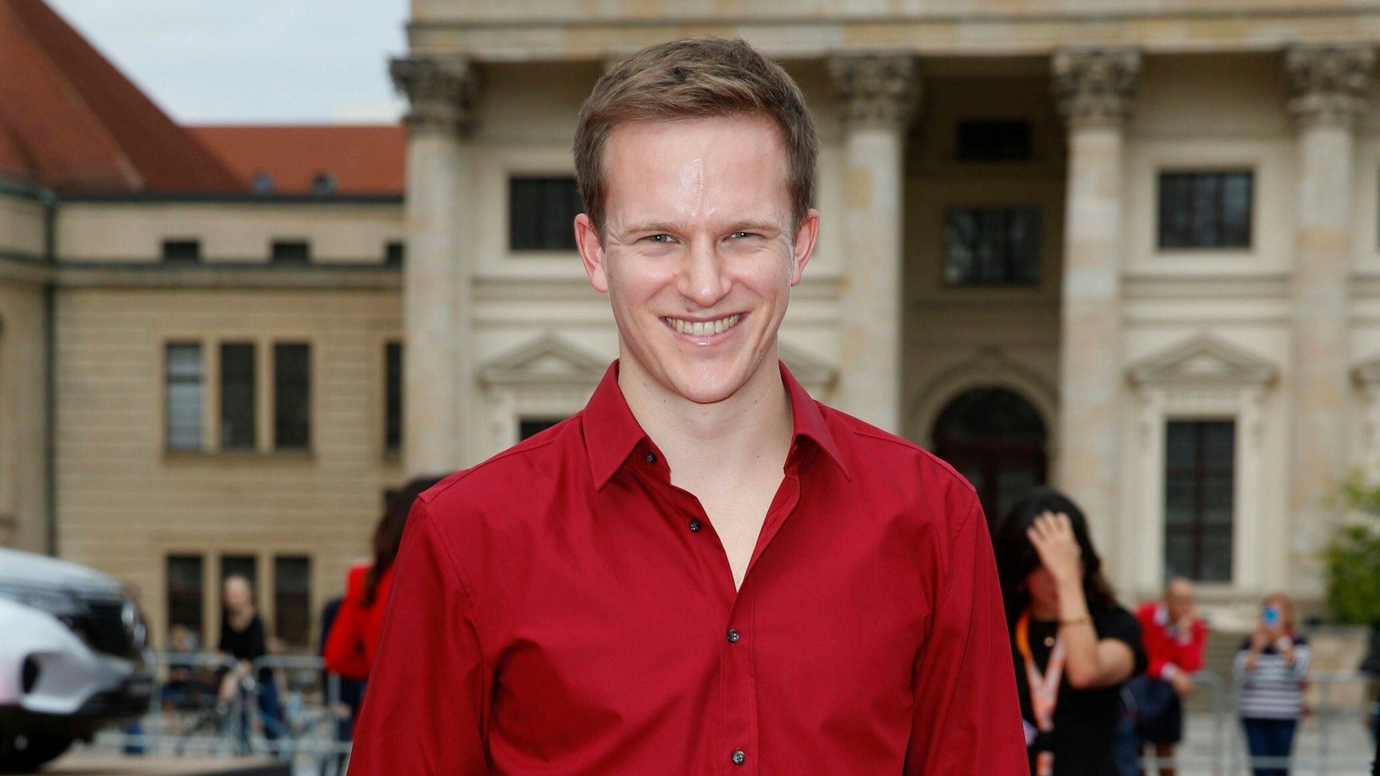 Der Marimbar-Spieler Christoph Sietzen steht am Gendarmenmarkt vor dem Berliner Konzerthaus. Er trägt ein leuchtend rotes Hemd und lacht.