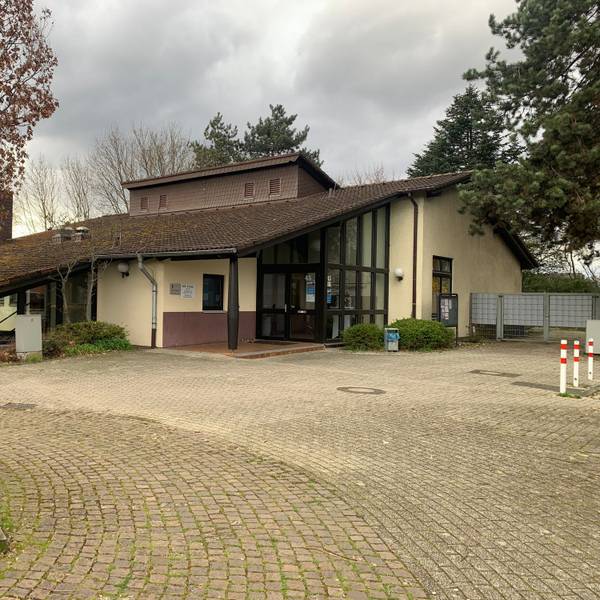 An einem gepflasterten Platz steht ein Gebäude mit einem heruntergezogenen Dach.