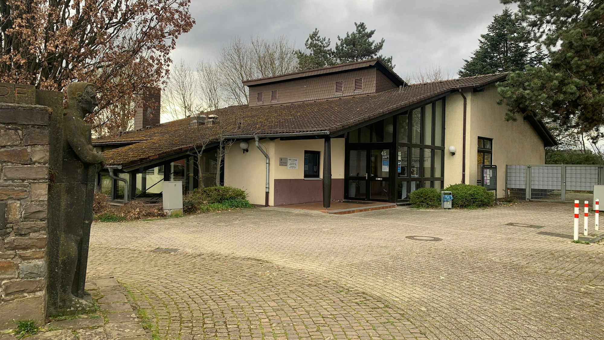 An einem gepflasterten Platz steht ein Gebäude mit einem heruntergezogenen Dach.