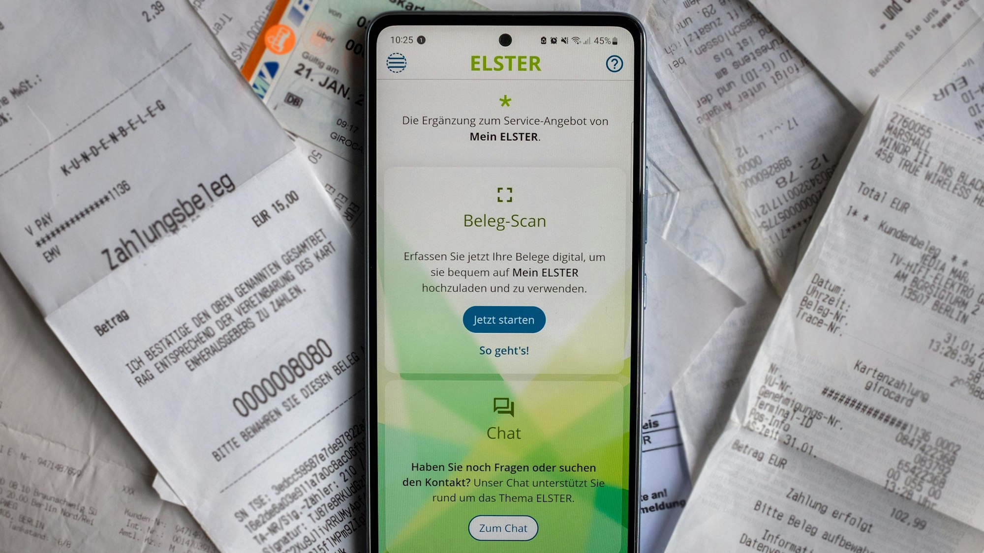 Ein Smartphone mit der geöffneten App „MeinELSTER+“ liegt auf einem Haufen Papierbelege.