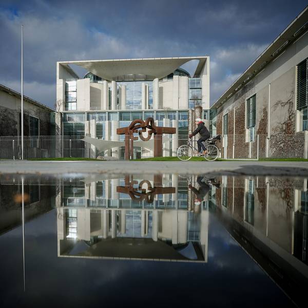 Das Bundeskanzleramt wird von der Sonne am Morgen unter dunklen Wolken angestrahlt.