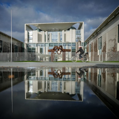 Das Bundeskanzleramt wird von der Sonne am Morgen unter dunklen Wolken angestrahlt.