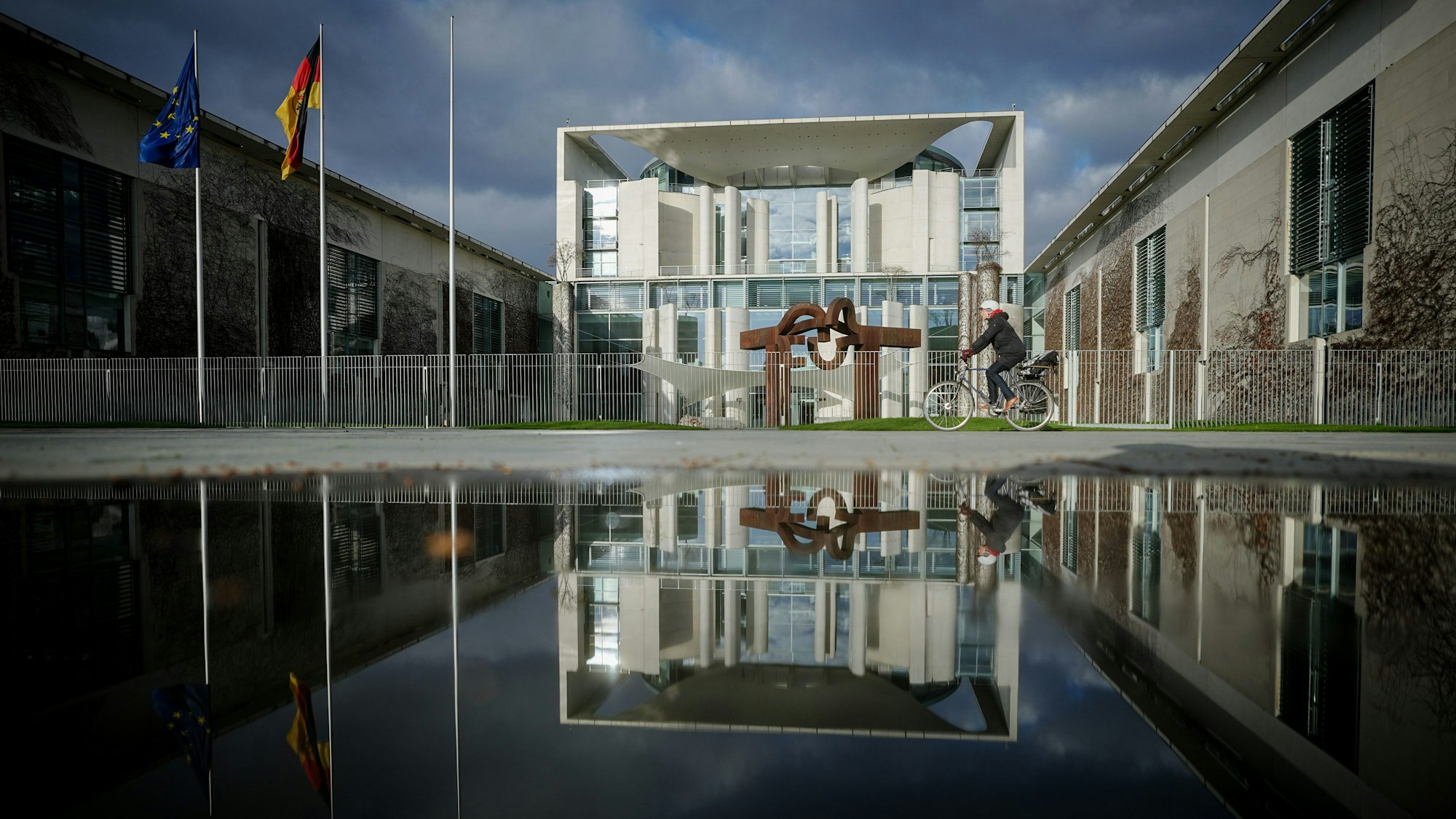 Das Bundeskanzleramt wird von der Sonne am Morgen unter dunklen Wolken angestrahlt.