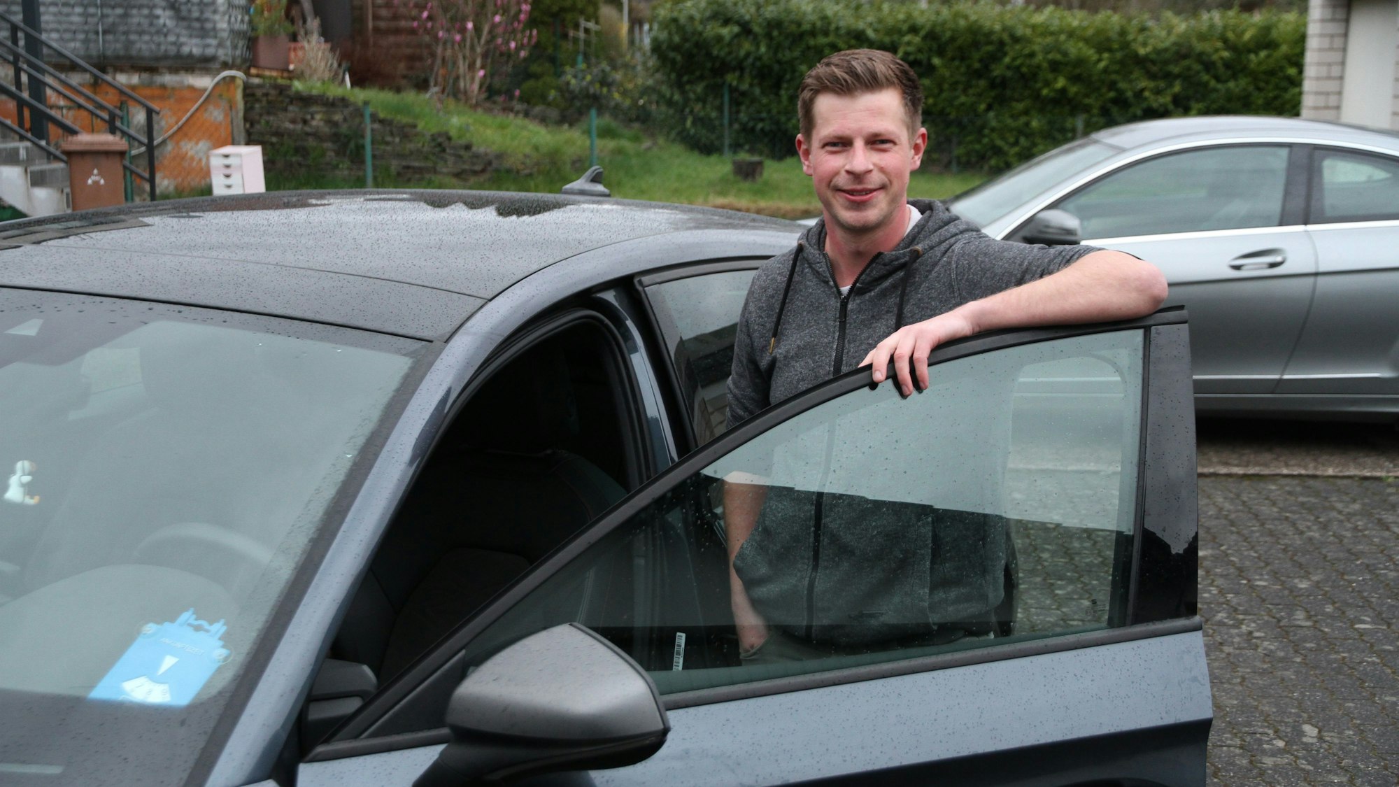Ein junger Mann steht an der geöffneten Fahrertür seines Pkw.