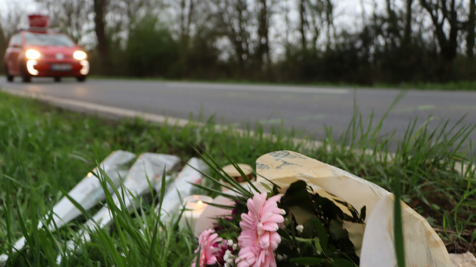 Auf dem Foto ist die Unfallstelle in Wesseling zu sehen. Am Straßenrand liegen Blumen, daneben stehen Kerzen.