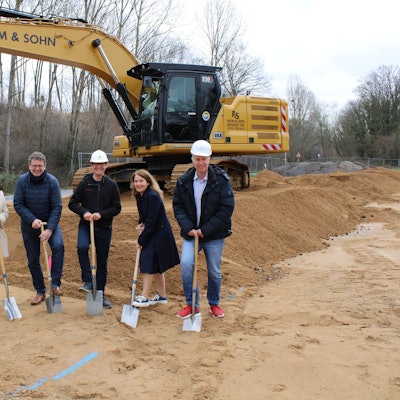 Die fünf Personen stehen vor einem Bagger und halten Spaten in der Hand.