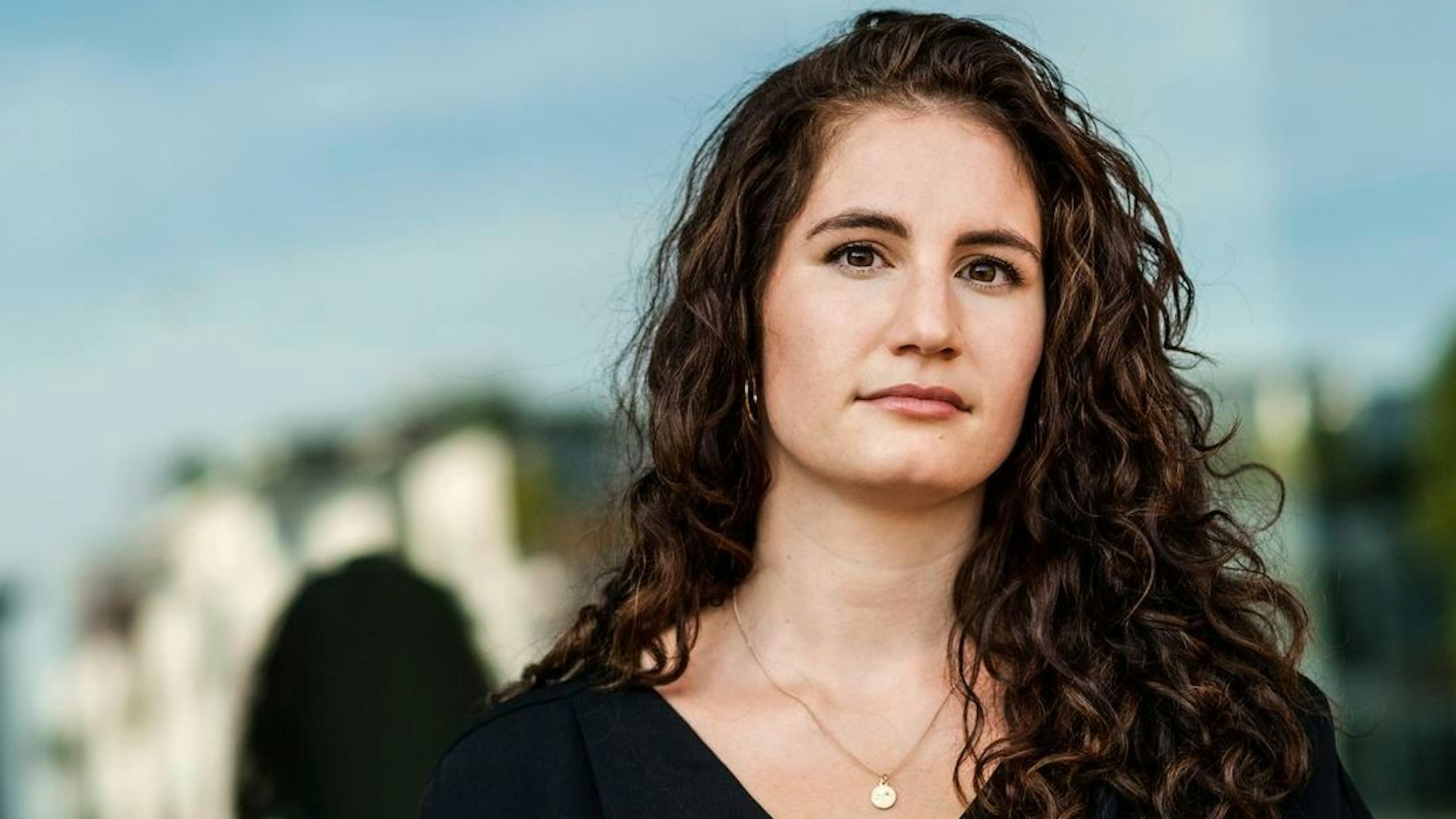 Autorin Lisa Roy hat lange gewellte braune Haare und dunkle Augen. Der Hintergrund ist verschwommen.