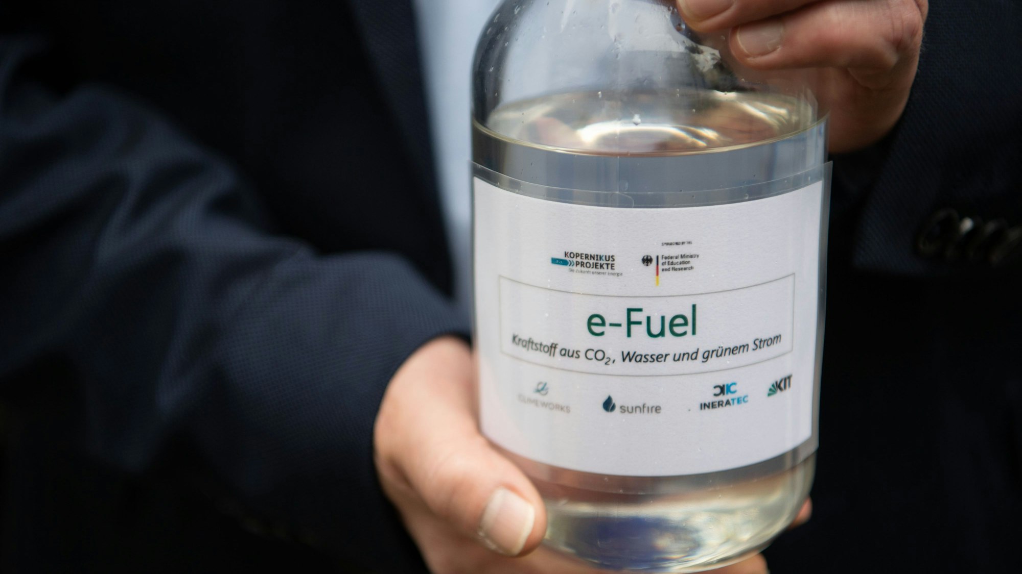 Ein Mitarbeiter einer Karlsruher Forschungsanlage hält eine Flasche mit E-Fuel. Der Kraftstoff soll trotz des Verbots für Verbrennungsmotoren eine Alternative sein.
