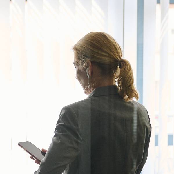 Eine Frau steht in einem Büro und schaut auf ihr Smartphone.