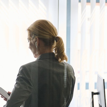 Eine Frau steht in einem Büro und schaut auf ihr Smartphone.
