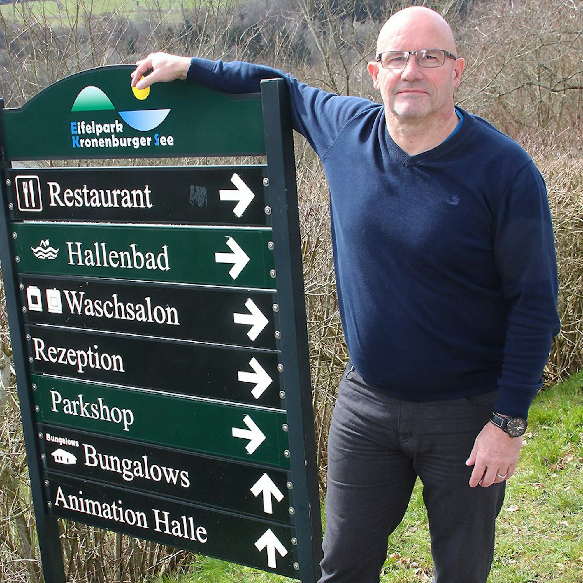 Detlef Feld steht neben einem Schild mit Wegweisern.