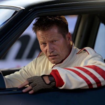 Til Schweiger sitzt im Auto und schaut in Richtung der Kamera, den linken Arm hat er am heruntergekurbelten Fenster.