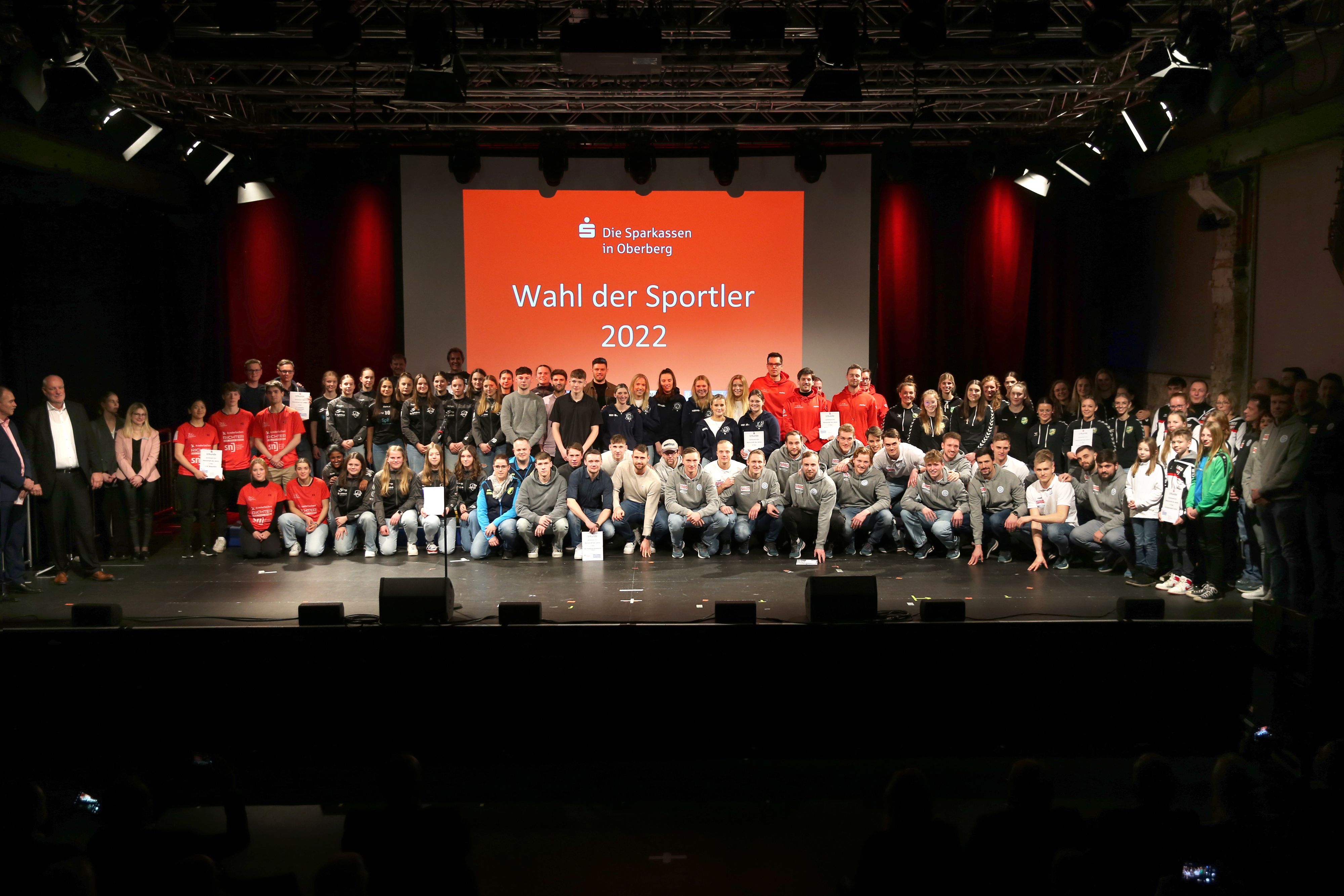 Auf einem Gruppenbild stehen zahlreiche Sportmannschaften vor einer roten Leinwand mit dem Logo der Sparkassen aus Oberberg und der weißen Aufschrift „Wahl der Sportler 2022“.