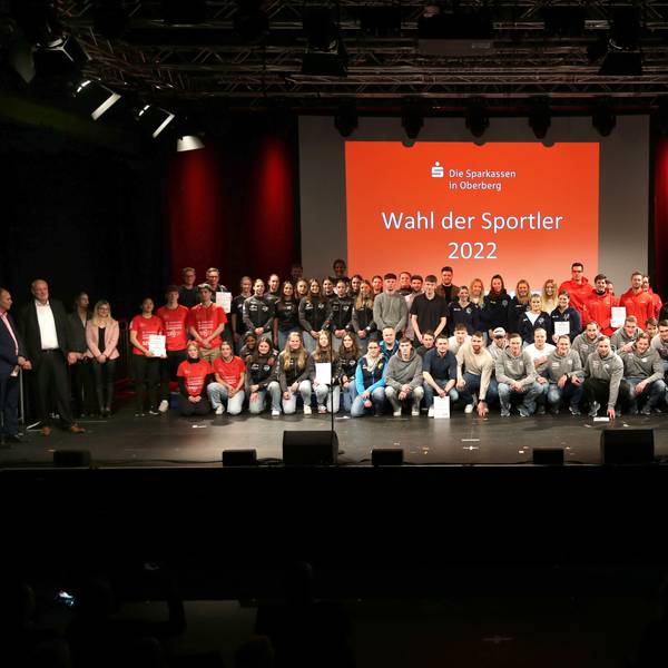 Auf einem Gruppenbild stehen zahlreiche Sportmannschaften vor einer roten Leinwand mit dem Logo der Sparkassen aus Oberberg und der weißen Aufschrift „Wahl der Sportler 2022“.