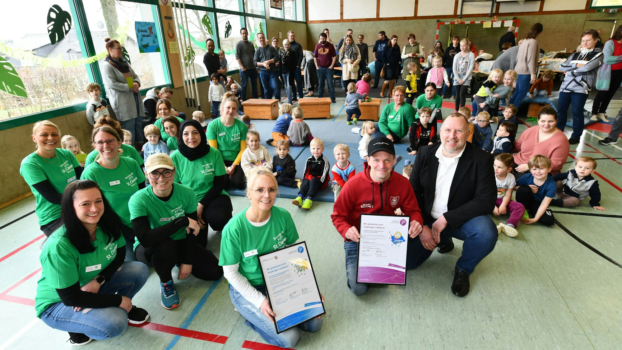 Kinder und Erwachsene sitzen auf dem Boden, zwei haben Urkunden in der Hand.