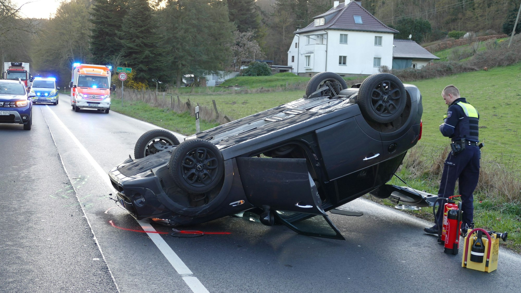 Ein Pkw liegt auf dem Dach auf der Straße. Im Hintergrund sind Rettungswagen und Polizei mit Blaulicht zu sehen.