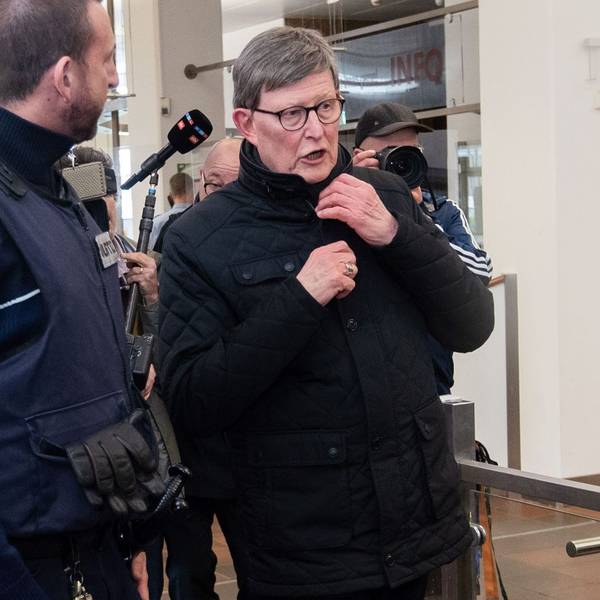 Kardinal Rainer Woelki wird im Foyer des Landgerichts von einem Justizbeamten zur Sicherheitsschleuse begleitet.