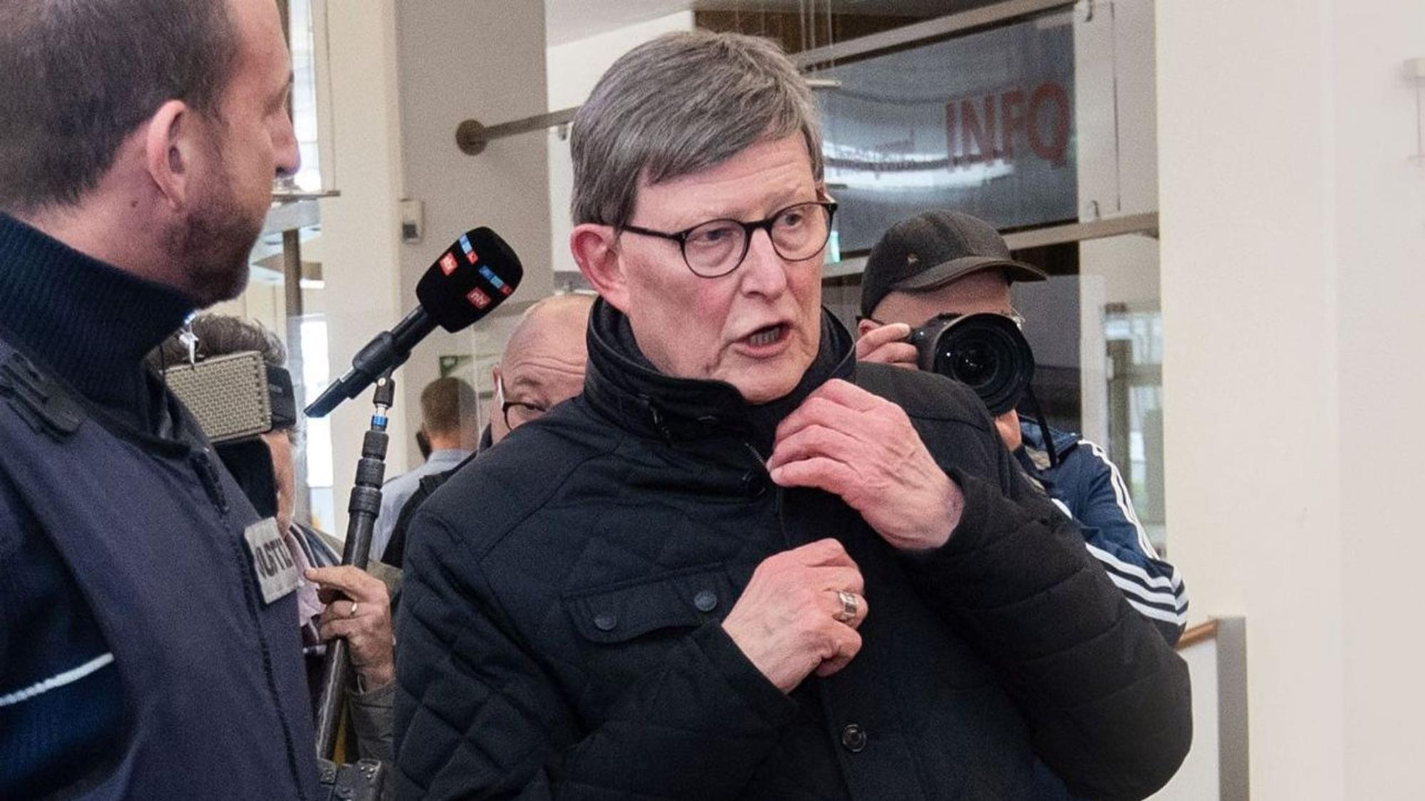 Kardinal Rainer Woelki wird im Foyer des Landgerichts von einem Justizbeamten zur Sicherheitsschleuse begleitet.