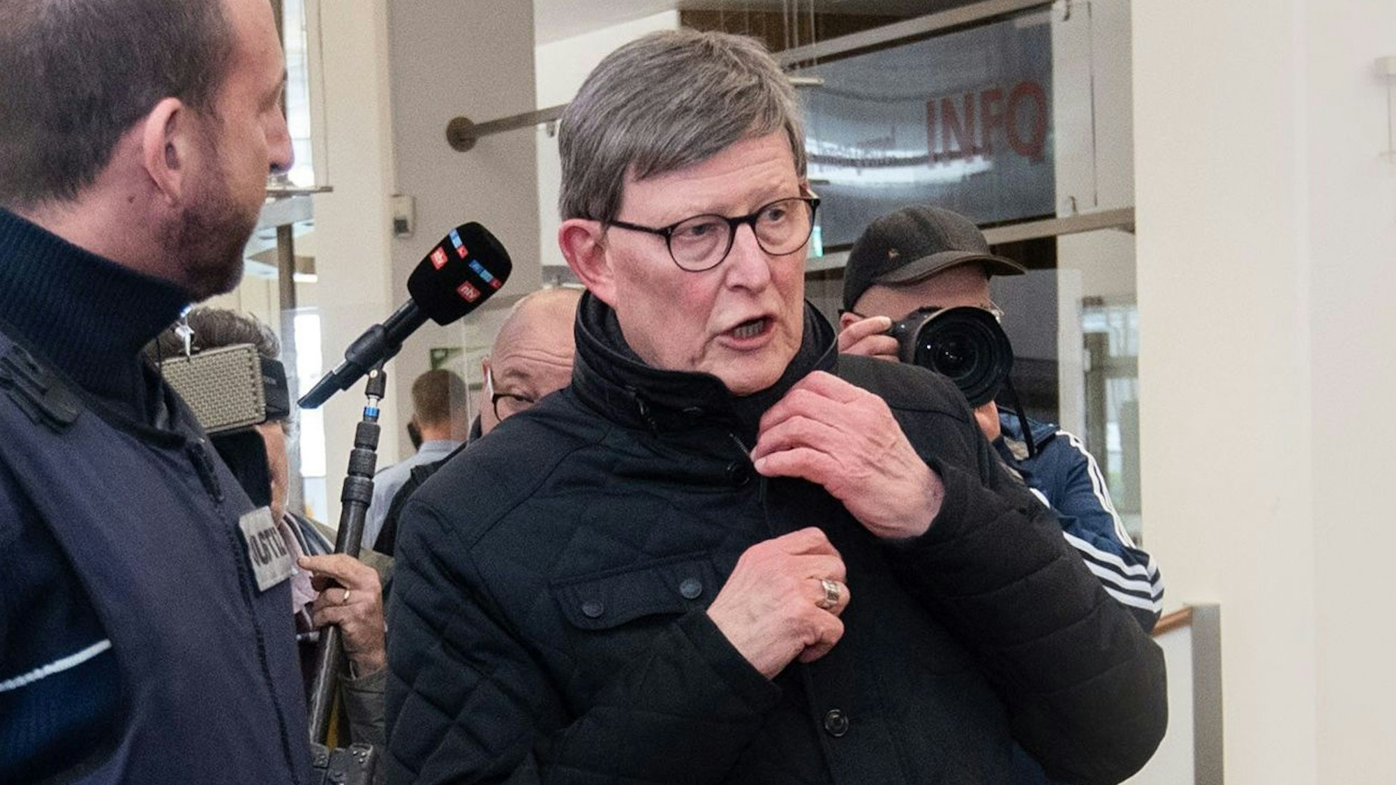 Kardinal Rainer Woelki wird im Foyer des Landgerichts von einem Justizbeamten zur Sicherheitsschleuse begleitet.
