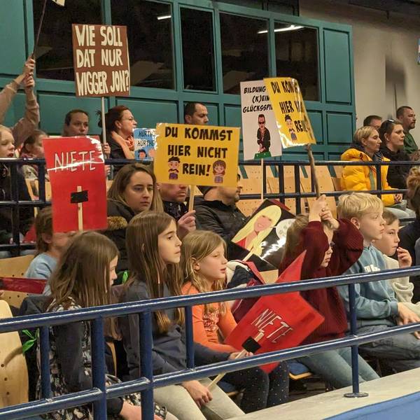 Kinder und Eltern zeigen Protestplakate auf den Zuschauerrängen.