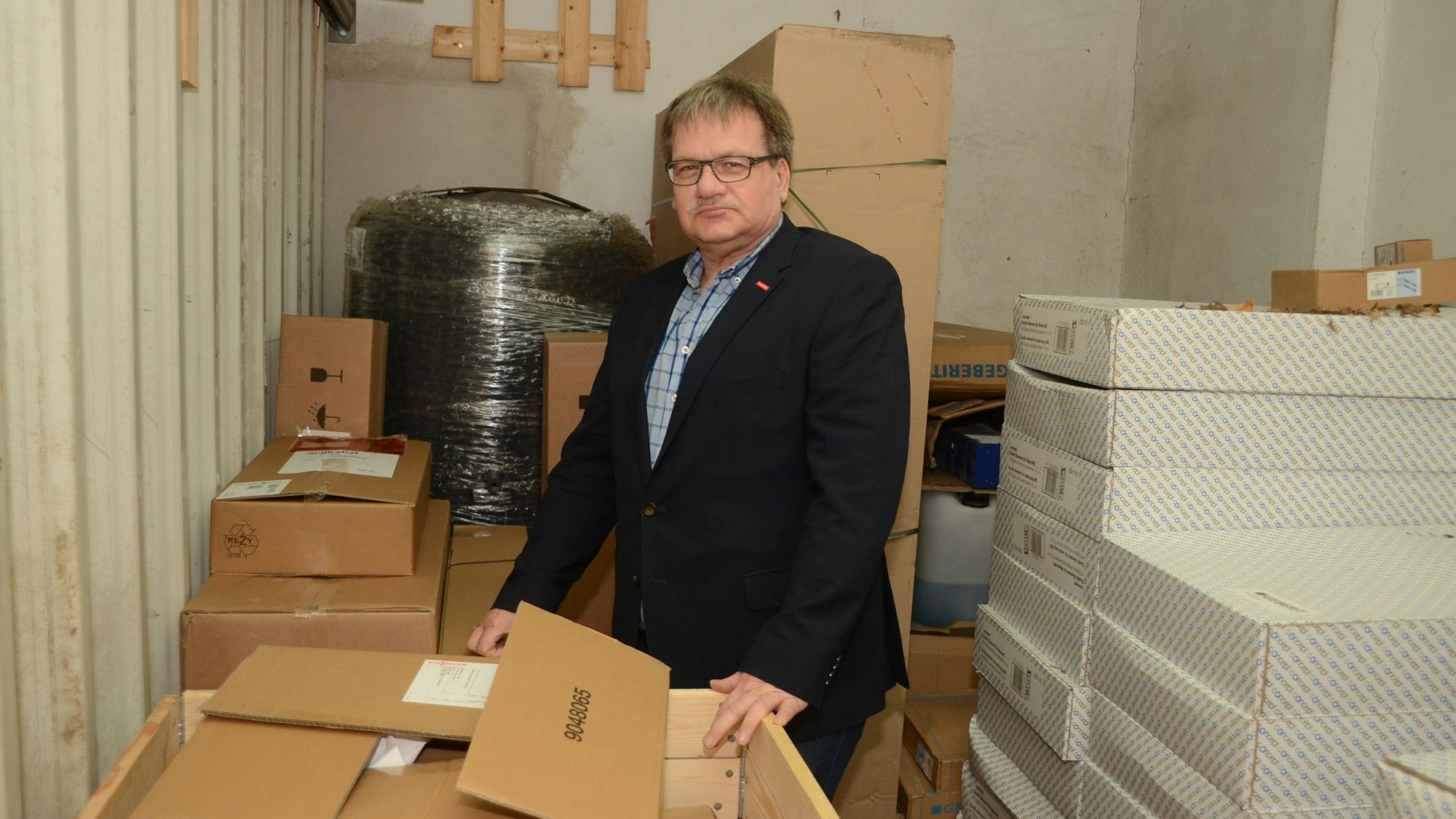 Guido Odenthal steht in einer Garage zwischen gestapelten Kisten.