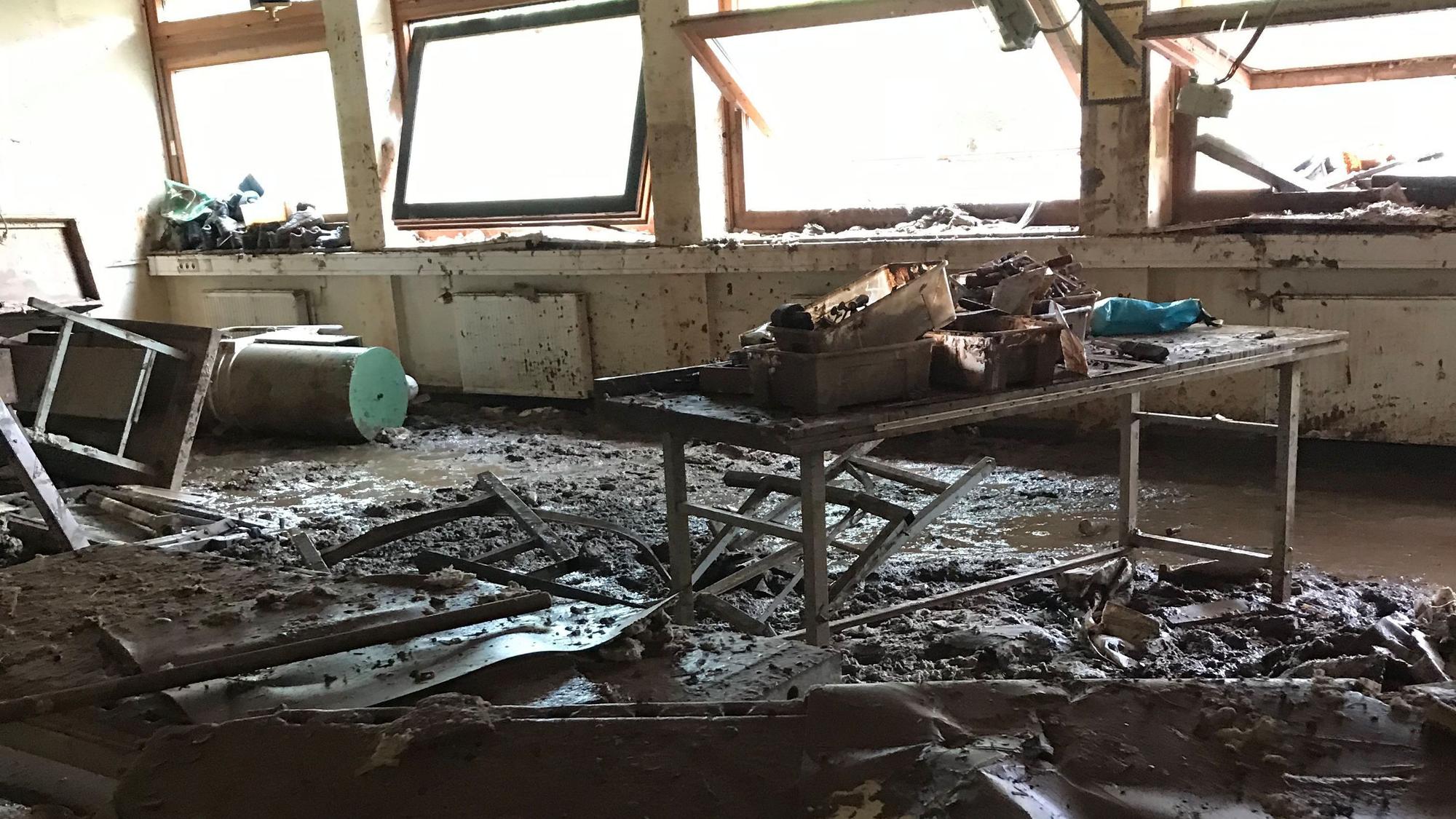Ein Klassenzimmer des Thomas-Eßer-Berufskolleg in Euskirchen, das von der Flut schwer beschädigt wurde. Der Boden ist mit Matsch bedeckt und die Fenster sind kaputt.