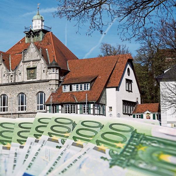 Hundert-Euro-Scheine aufgefächert im Vordergrund, im Hintergrund das Rathaus in Bergisch Gladbach.