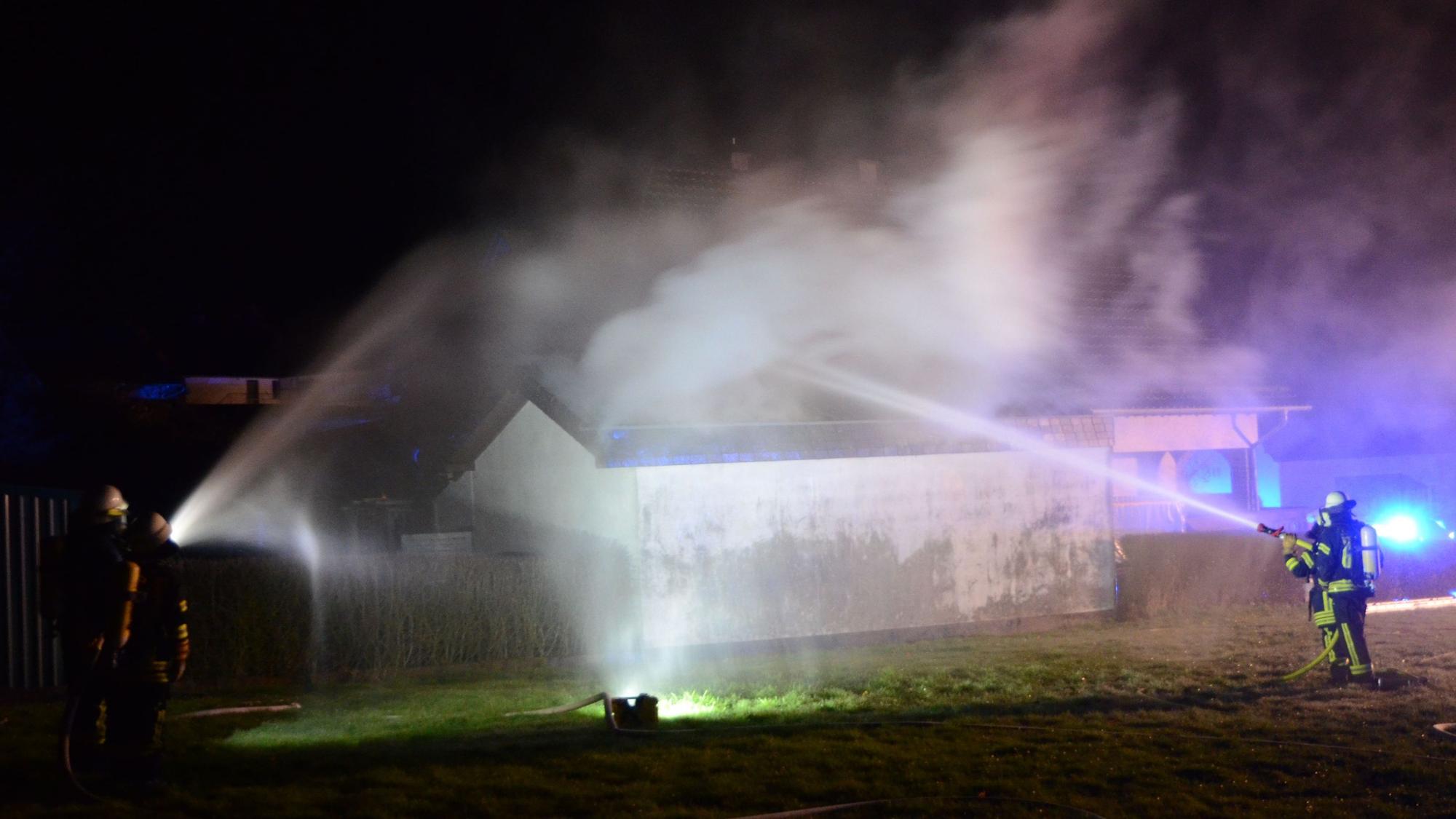 Feuerwehrleute löschen in der nächtlichen Dunkelheit den Garagenbrand.